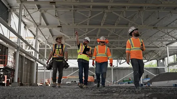 Construction crew in hard hats and high-visibility gear walking through a steel-framed building under construction