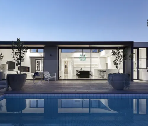 Modern design-build home with floor-to-ceiling glazing and a pool at dusk