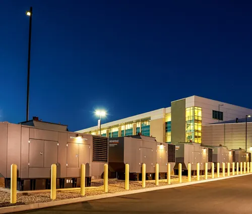Row of industrial backup generators outside a commercial facility at night