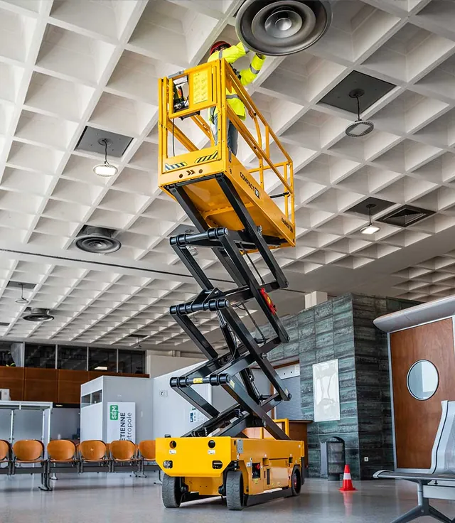 Technician on a scissor lift installing ceiling equipment inside a commercial building